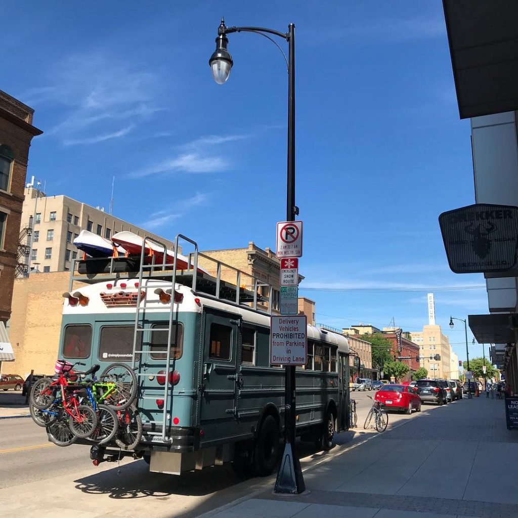Photo of a large skoolie parked in a downtown area. 