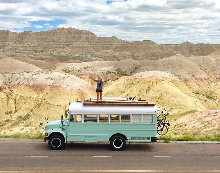 Woman standing on the roof of her skoolie in front of Badlands National Park. 