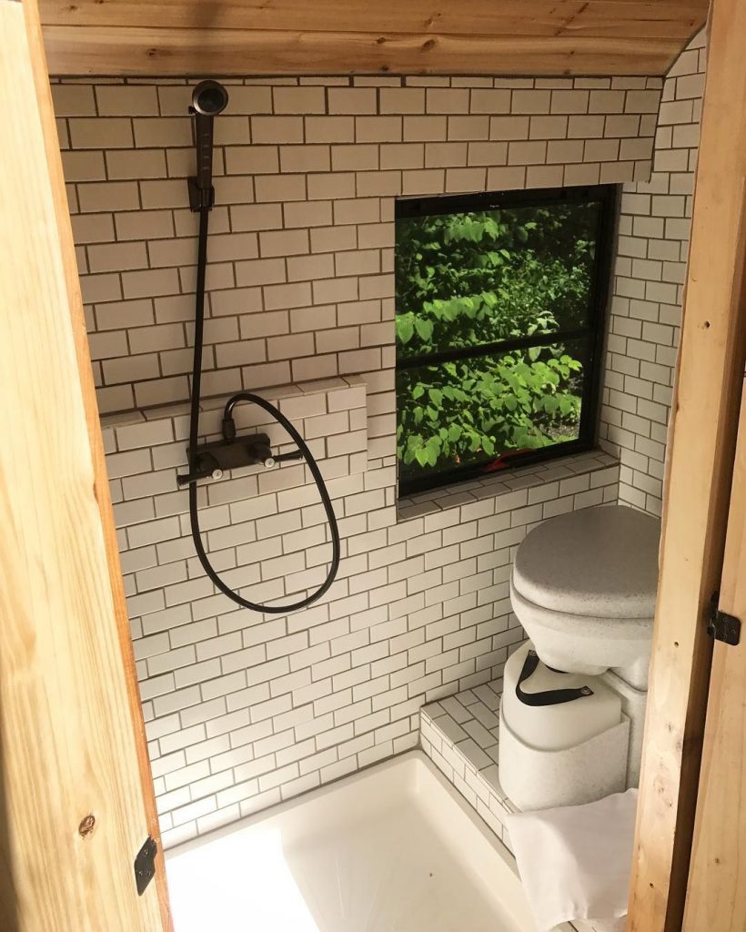 White tiled skoolie bathroom with a composting toilet and shower. 