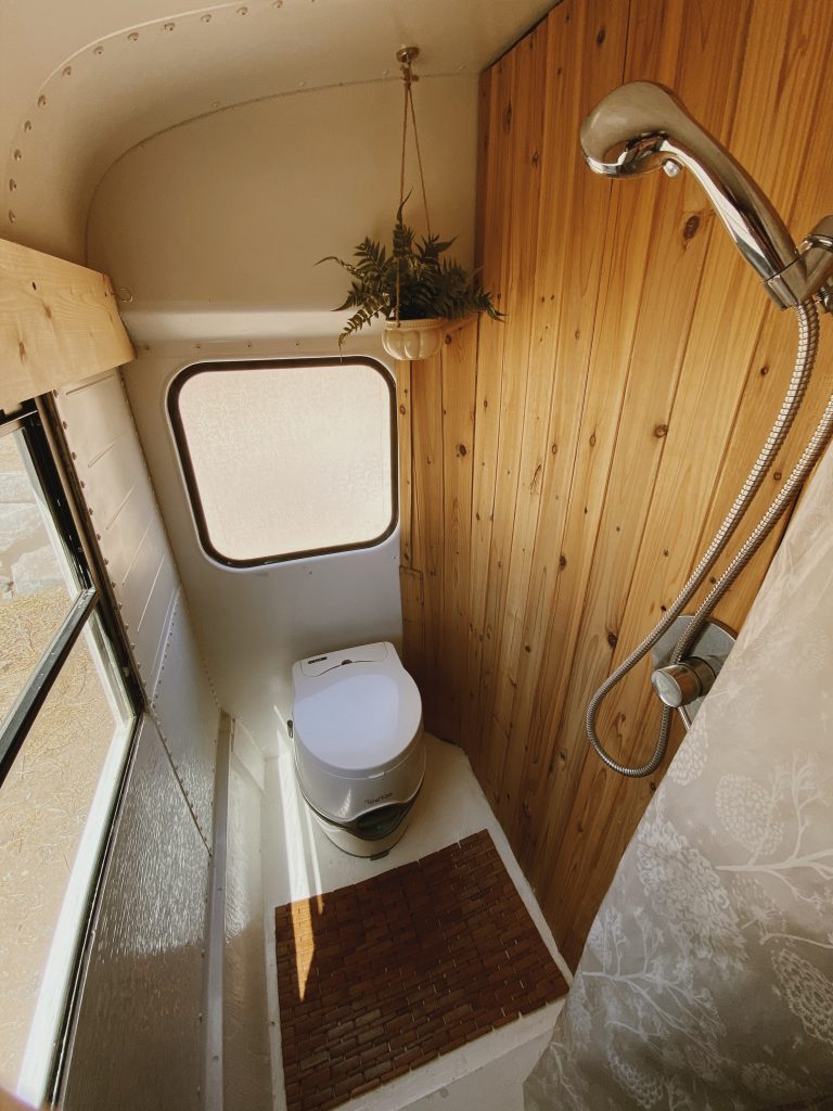 Skoolie bathroom with wood paneling, plant, and natural light. 