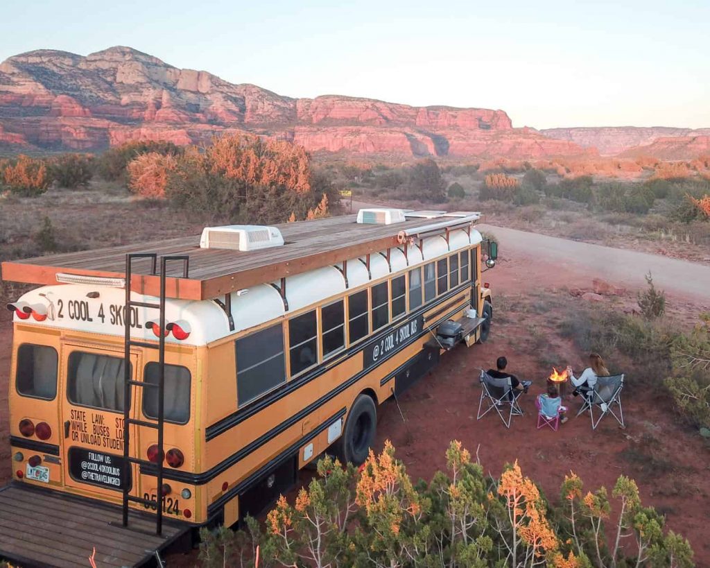 The Traveling Red skoolie parked outside with scenic red cliffs in the background. 