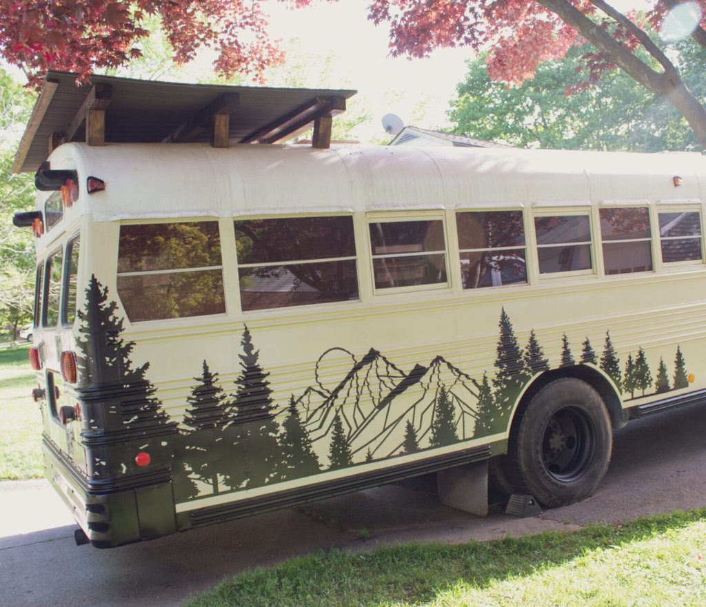 Photo of Time to Go Adventure's skoolie which is white with mountains and trees painted on it in a dark color. 
